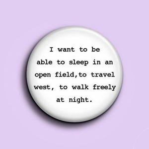 Könnte beinhalten: Ein weißer Knopf mit dem Text "I want to be able to sleep in an open field, to travel west, to walk freely at night" in Schwarz, vor einem hellvioletten Hintergrund.