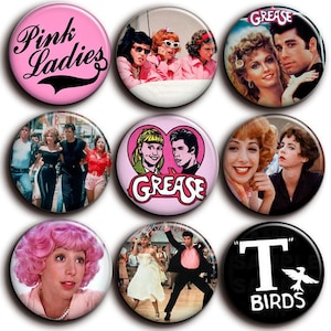 Peut inclure: Neuf badges ronds avec des images et du texte du film Grease. Les badges incluent des images des Pink Ladies, le mot "Grease" et d'autres personnages. Les badges sont de différentes couleurs, dont le rose et le noir.