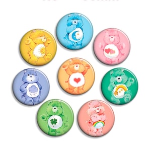 Op de afbeelding: Een set van acht ronde buttons met gekleurde Care Bear-personages. Elke button toont een unieke beer met een specifiek symbool op de buik, waaronder motieven zoals een zon, maan, harten, wolk, regenboog, klaverblad en sterren in diverse kleuren.