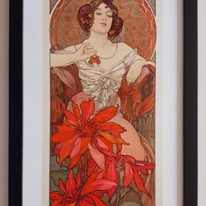 Könnte beinhalten: Gerahmter Kunstdruck mit einer sitzenden Frau mit roten Haaren und Schmuck vor einem verzierten Hintergrund. Große rote Blumen befinden sich im Vordergrund. Der Druck ist in einem schwarzen Rahmen.