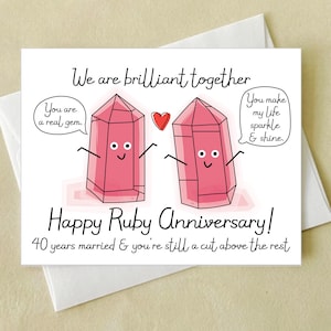 May include: A white greeting card featuring two cartoon pink ruby crystals with faces and arms. Text reads: We are brilliant together, You are a real gem, You make my life sparkle & shine, Happy Ruby Anniversary! 40 years married & you're still a cut above the rest.