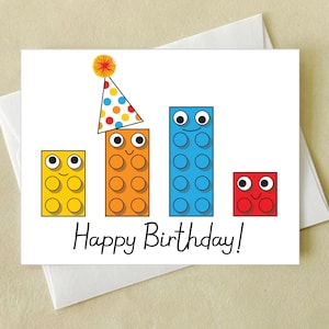 May include: A birthday card with a colorful block design. The blocks have happy faces and one block is wearing a party hat. The card says "Happy Birthday!"