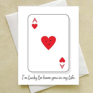 May include: A white greeting card featuring a playing card design, the Ace of Hearts. The card has a red heart with a smiling face in the center and the text "I'm lucky to have you in my life."