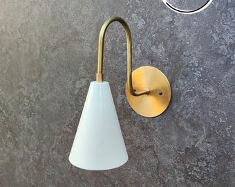 May include: A gold wall sconce with a white cone-shaped shade. The sconce has a curved arm and a round back plate.