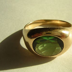 Könnte beinhalten: Ein goldener Ring mit einem großen, runden, grünen Edelstein, der in der Mitte eingesetzt ist.