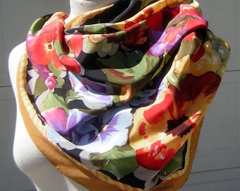 May include: A black silk scarf with a floral print of red, yellow, purple, and green flowers. The scarf has a gold rope trim and the text "Cardin" is visible in the bottom right corner.