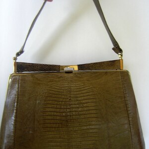 May include: A brown leather handbag with a gold clasp and a long strap. The bag has a textured, snakeskin-like pattern.