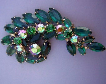 Pode incluir: Um broche verde e iridescente de strass em forma de ramo com folhas. O broche é feito de metal dourado e apresenta uma variedade de tamanhos e formas de strass.