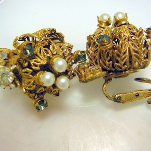 Könnte beinhalten: Ein Paar goldfarbene Ohrclips mit floralem Design. Die Ohrringe sind mit Perlenimitationen und blauen Strasssteinen besetzt.