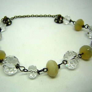 Op de afbeelding: Een delicate ketting gemaakt met heldere gefacetteerde glazen kralen en lichtgroene opalescente kralen. De kralen zijn verbonden met draad en een klein kettinkje.