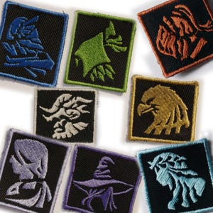 May include: A selection of embroidered patches, each with a different fantasy-themed design. The patches feature symbols like an eagle and a wizard's hat, in colours such as blue, green, and orange, set against a black background.