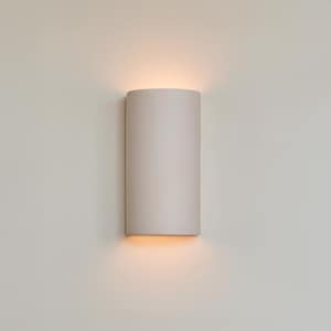 May include: A cylindrical, off-white wall sconce emits a warm, downward glow. The fixture is mounted on a light-coloured wall, creating a soft, ambient light. The design is minimalist and modern, suitable for various interior styles.