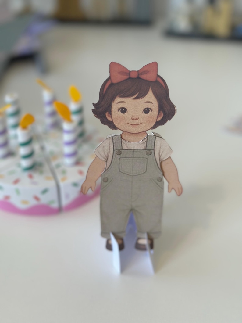 Pode incluir: Recorte de papel de uma menina de desenho animado com cabelo castanho e um la&ccedil;o vermelho. Ela usa uma camisa branca e macac&atilde;o cinza. Um bolo de anivers&aacute;rio com velas est&aacute; no fundo.