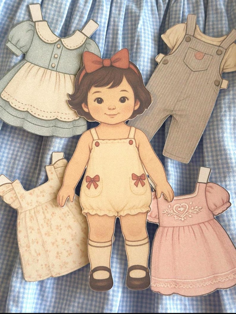 Pode incluir: Uma boneca de papel com um macac&atilde;o creme e um la&ccedil;o vermelho, rodeada de roupas de papel. As roupas incluem um vestido azul claro, macac&atilde;o, um vestido floral e um vestido rosa com um cora&ccedil;&atilde;o. O fundo &eacute; um padr&atilde;o xadrez azul e branco.