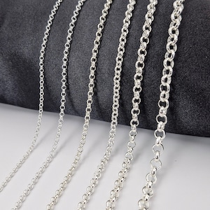 Puede incluir: Un conjunto de seis cadenas de plata de diferentes grosores, mostradas sobre un fondo de tela negro.