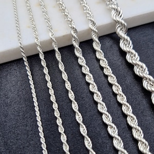 May include: A set of seven silver rope chains of varying thicknesses, laid out on a white surface and a black surface.