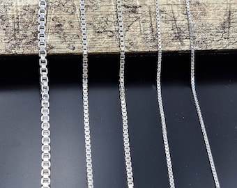 May include: A set of seven silver chains of varying lengths, displayed against a wooden background and a black surface.