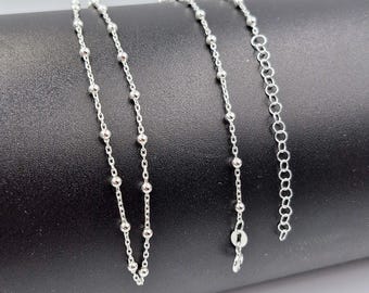 May include: A silver chain necklace with small round beads. The chain is on a black surface.