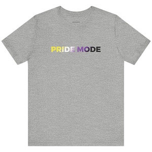 May include: A heather gray t-shirt with the text "PRIDE MODE" in a gradient of yellow, white, purple, and black. The shirt is a short-sleeved crew neck style.