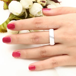 May include: White ceramic ring with a row of small clear stones on the band.  "PRIDE MODE" is visible in the background.