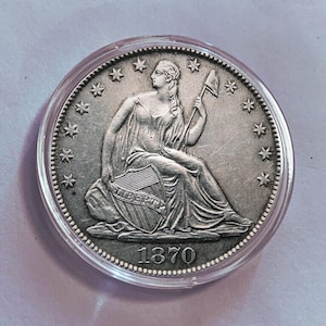 Op de afbeelding: Zilveren Amerikaanse Trade Dollar-munt uit 1870, met een zittend Vrijheidsbeeld dat een bundel pijlen en een schild met de inscriptie "LIBERTY" vasthoudt. De munt is omgeven door een ring van 13 sterren.