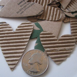 May include: A close-up of a pile of brown cardboard hearts, some with text that reads "Same green because this 85% post-consumer uses 34% less paper" and "use only". A US quarter is in the foreground.