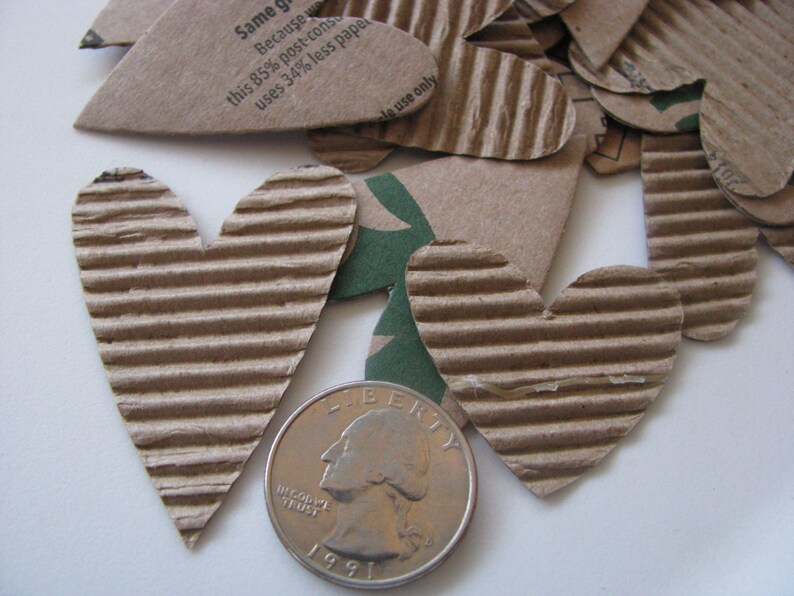May include: A close-up of a pile of brown cardboard hearts, some with text that reads "Same green because this 85% post-consumer uses 34% less paper" and "use only". A US quarter is in the foreground.