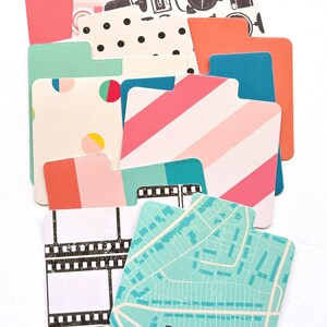 Könnte beinhalten: Eine Sammlung farbenfroher Karteikarten mit Mustern. Designs umfassen Polka Dots, Streifen, Filmstreifen, Karten und Kamera-Illustrationen. Die Karten sind in den Farbtönen Rosa, Blau, Orange und Grün gehalten, mit weißem Hintergrund.