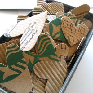 May include: A collection of brown cardboard hearts with green printed text. The text includes "Same great sleeve", "Because we care about", "this 85% post-consumer", "uses 34% less", "Do", "Custom", "Drink", and "Same great sleeve".