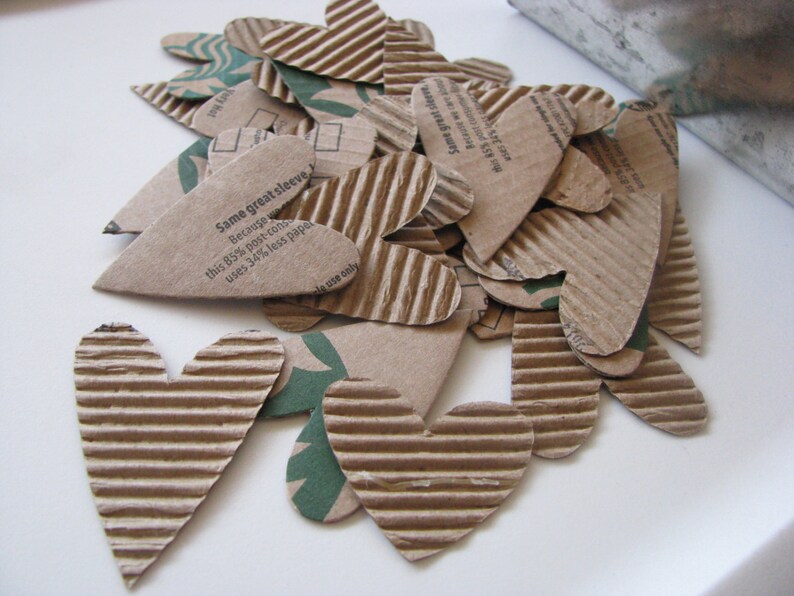 May include: A pile of brown cardboard hearts with a white background. The hearts have a corrugated texture and some have text printed on them that reads "Same great sleeve Because this 85% post-con uses 34% less pape le use only".