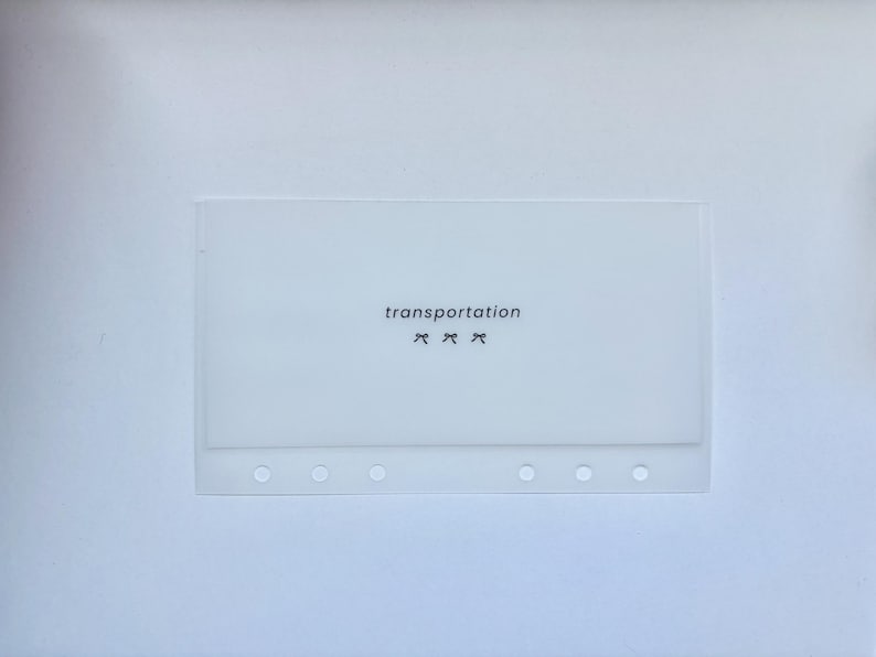 May include: A translucent white planner pocket with the word "transportation" printed in black, along with three small bow graphics. The pocket has six circular holes along the bottom edge.