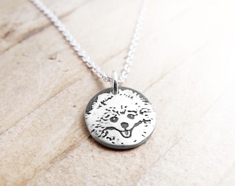May include: A silver necklace with a round pendant featuring a detailed etched image of a fluffy dog's face.