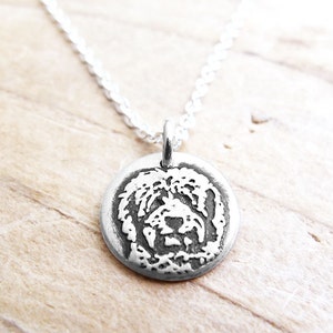 Peut inclure: Un collier en argent avec un pendentif rond représentant une image en relief détaillée d'un visage de chien.