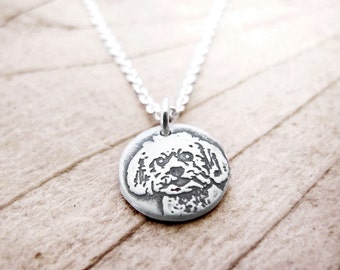 May include: A silver necklace with a round pendant featuring a detailed engraved image of a white dog's face.