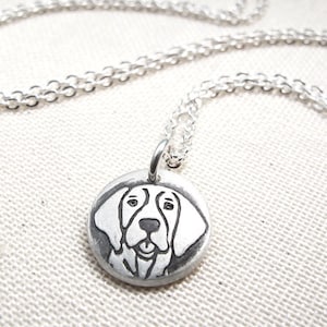 May include: A silver necklace with a round pendant featuring a black and white line drawing of a dog's face.