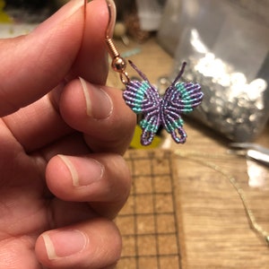 May include: A purple and teal butterfly-shaped earring with a copper hook.