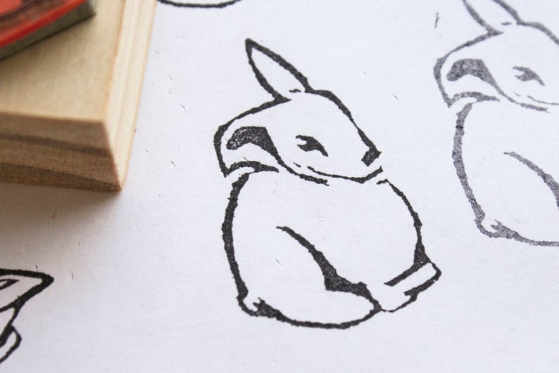 May include: A black and white line drawing of a rabbit sitting with its head tilted to the side. The rabbit is drawn in a simple, cartoon style.