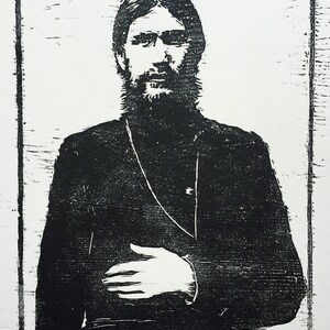 以下が含まれることがあります： 長いひげと黒い服を着た男性の白黒木版画。肖像画は太い黒い縁で囲まれています。男性は正面を向き、右手を胸に当てています。