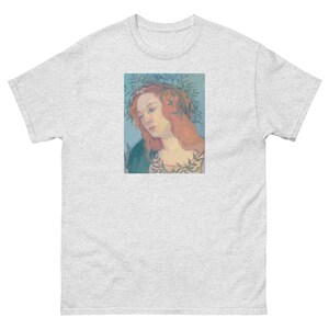 An off white color cotton tshirt. Art on a tshirt, a portrait painting of the Goddess Minerva. The painting is a neoclassical style, with the goddess art centered on the shirt.