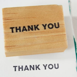 May include: A wooden stamp with the text "THANK YOU" printed in black ink.