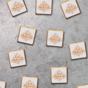 May include: A collection of ten square chocolate bars with gold foil wrappers. Each bar has a white label with the text "Eid Mubarak" in gold calligraphy.