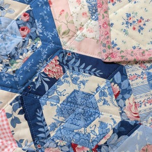 Nostalgic hexagon baby quilt with mostly delicate floral prints in calm shades of blue, pink and cream, all cotton, machine washable.