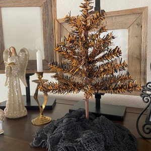 May include: A small, orange and black artificial Christmas tree with a black mesh fabric base. The tree is on a wooden surface with other decorative items.