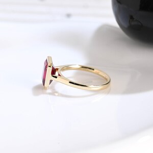 Puede incluir: Un anillo de oro con una piedra preciosa rectangular de color rojo intenso montada en orientaci&oacute;n vertical. La banda es lisa y pulida, mostrando un engaste de metal sencillo que sujeta firmemente la piedra roja desde el perfil.