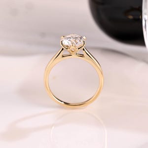 May include: A gold engagement ring with a round, clear diamond set in a prong setting. The ring has a simple band.
