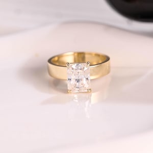 May include: A gold ring with a large, clear, square-shaped diamond.