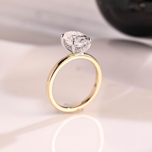 May include: A gold engagement ring with a large oval-shaped diamond set in a pave setting. The band is thin and has a polished finish.