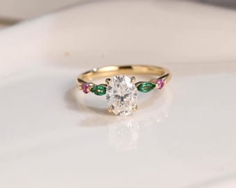 Könnte beinhalten: Ein goldener Ring mit einem ovalen Diamanten als Mittelstück und kleineren grünen und rosa Steinen auf der Ringschiene.