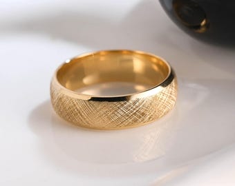 May include: A gold-toned ring featuring a textured, cross-hatched finish on the outer band. The ring has a smooth, polished interior surface and a rounded profile, showcasing a metallic luster that reflects light across its detailed surface.
