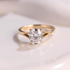 Könnte beinhalten: Ein goldener Verlobungsring mit einem großen, klaren ovalen Diamanten, der in einer geteilten Schiene sitzt.